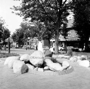 Rathausvorplatz [späterer Europaplatz]: Springbrunnen aus Findlingen: dahinter Poststraße mit Geschäften und Fußgängern