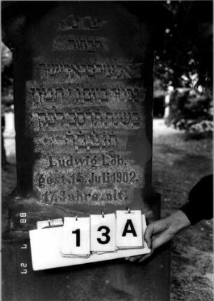 Grabstein 13 (Index: 100110215) Material: Sandstein Zustand: verwittert Maße HxBxT: 135x73x45 cm Beschreibung: Stele, getreppter Sockel, giebelartiger Abschluß mit Verdachung: Grabstein 13A