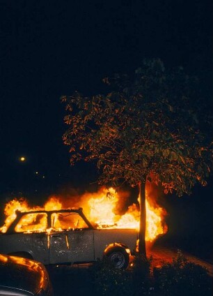 Rostock-Lichtenhagen. Brennender Trabi unter einem Baum, nach Strassenschlachten mit der Polizei