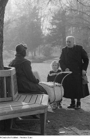 Eine Frau mit Mädchen an der Hand sowie eine Frau auf einer Parkbank mit Kinderwagen