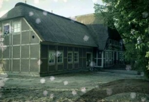 Papierholz 1: Gaststätte Zur Hahnheide: giebelständiges Bauernhaus mit Reetdach: Teilansicht: Straßenfront mit Fachwerk: rechts Altbau, davor Terrasse mit Geländer: links neuer Querbau bei Fertigstellung, Traufseite mit Tür, Giebelseite