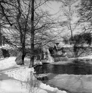 Mühlenteich: Wehr mit Überlauf: vorn links und hinten rechts Bäume: Winter