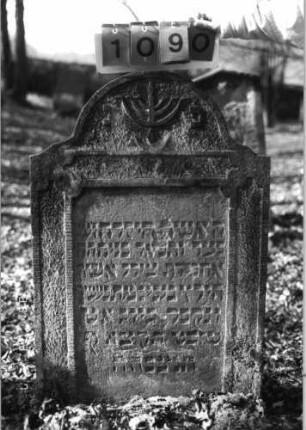 Grabstein 1090 (Index: 99753295) Material: Sandstein Zustand: leicht beschäd/verwitt/Textverlust Maße HxBxT: 104x69x10 cm Beschreibung: Stele, eingezog, Rundbogenabschluß, rechteck. Schriftfeld eingetieft Symbolik: Menora: Grabstein 1090