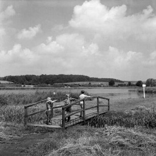 Herrenteich: Wanderweg nördlich der Wohnsiedlung Herrenhusen: drei Jungen auf Holzbrücke, mit Pfeil und Bogen: hinten rechts Hinweisschild: im Hintergrund Westufer