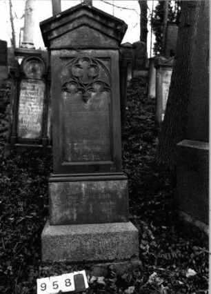 Grabstein 958 (Index: 99802656) Material: Sandstein Zustand: leicht verwittert Maße HxBxT: 210x57x45 cm Beschreibung: mehrfach getreppter Sockel, Stele mit verdachtem Giebel Symbolik: Inschriftenfeld mit gotisierendem Maßwerk: Grabstein 958