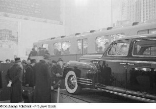 Besucher vor einem Automobil, im Hintergrund ein Triebwagen