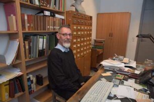 Porträt Perk Loesch, Fachreferent der SLUB : Porträt des Kunstwissenschaftlers Perk Loesch, Fachreferent und von 1996 bis 2019 Leiter der Handschriftenabteilung an der Sächsischen Landesbibliothek – Staats- und Universitätsbibliothek Dresden (SLUB). Aufnahme in seinem Dienstzimmer am Schreibtisch