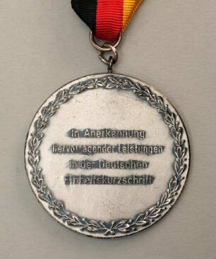 Silbermedaille Deutsche Meisterschaften in Kurzschrift und Maschinenschreiben in Göttingen 1975 am schwarz-rot-goldenen Band : Sammlung Deutscher Stenografenbund. Silbermedaille Deutsche Meisterschaften in Kurzschrift und Maschinenschreiben in Göttingen 1975 am schwarz-rot-goldenen Band. Messing, versilbert; Durchmesser 50 mm, Gewicht 50 g (1975; Deschler & Sohn, München). Dresden: SLUB R c 0521