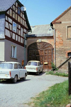 Einfahrt zu einem Vierseithof: Wohnhausecke und Hoftor; zwei PKW Trabant