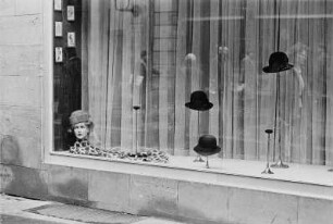 Schaufenster eines Hutgeschäfts mit sich in der Scheibe spiegelnden Passanten