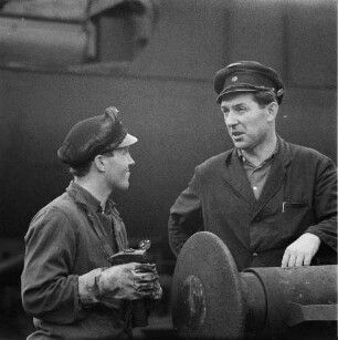 Zwei Eisenbahner zwischen Gleisen im Gespräch, im Vordergrund ein Hülsenpuffer (Serie Deutsche Reichsbahn - Brigade "Otto Buchwitz")