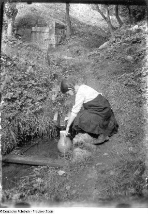 Mädchen an einer Quelle mit Krug beim Wasserholen (vermutlich die Tochter der Familie Müller in Rongstock)