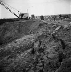 Industriestraße: Absackung eines Teilstücks: vorn Abbruchkante mit Grube: rechts Absperrung: dahinter Bagger, Arbeiter, Baubude, Baumaschinen und Pkw