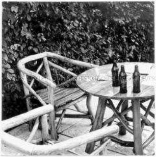 Zwei Holzstühle und ein Holztisch mit drei Bierflaschen