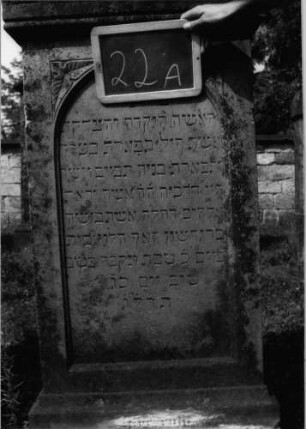 Grabstein 22 (Index: 99801897) Material: Sandstein Zustand: verwittert Maße HxBxT: 153x55x22 cm Beschreibung: Stele, Sockel, Rundbogengiebel mit Eckakroteren, eingetieftes Schriftfeld mit Rundbogen Symbolik: Eichblätter, Blätterornamentik auf dem Rundbogen: Grabstein 22A
