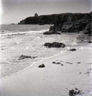 Strand in einer Bucht mit Felsen an der französischen Atlantikküste, an der Klippe ein Haus