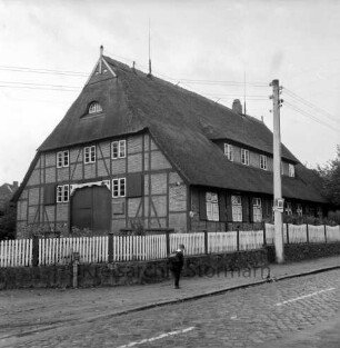 Dorfstraße mit Kopfsteinpflaster: Schullandheim "Heinrich-Sahrhage-Haus": davor Holzzaun: in der Mitte Schulkind: rechts Strommast