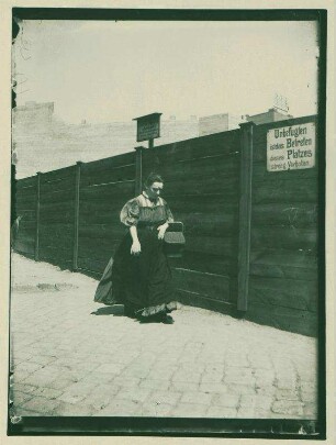 Frau mit Korb vor einem Bauzaun
