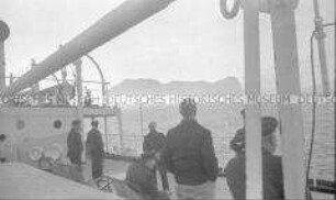Heimfahrt der Kriegsgefangenen vom Internierungslager "Angel Island" auf dem italienischen Dampfer "Fella", mehrere Personen an Deck, bei Sonnenuntergang gen Felsenküste blickend