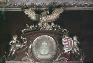 Türbekrönung mit einem Medaillon, das als Symbol den Reichsapfel zeigt, seitlich halten Putti das Wappen und die Krone Ungarns
