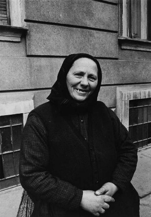 Alte Frau vor einer Hauswand
