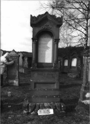 Grabstein 115 (Index: 100114783) Material: Sandstein und ? Zustand: leicht verwittert im Giebel Maße HxBxT: 244x68x32 cm Beschreibung: Ädikula, eingezogener Spitzbogen, Voluten und Akroter, Mohnkapseln im Giebel Symbolik: Mohnkapseln Besonderheit: kulturhistorisch wertvoll / künstl.-formale Gründe (allgemein): Grabstein 115
