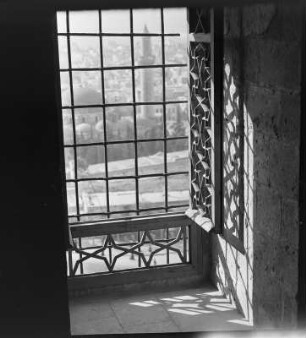 Blick durch ein vergittertes Fenster auf eine Stadt, im Mittelgrund eine Moschee