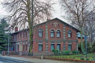 Alte Landstraße: traufständiges Bauernhaus aus Backstein mit umlaufendem Gesims: Giebelseite Wohntrakt, Quaderputz an Lisenen und über Fenstern: links Straßenfront, vorne Wohntrakt mit Eingangstür, hinten Wirtschaftstrakt, in Obergeschoss Schlitzfenster: davor Garten, Bäume, Gartenzaun
