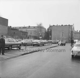 Hagenstraße: Parkplatz mit Pkws: links Fußgänger: hinten rechts Firmenschild der Volksbank Bad Oldesloe: links Rückfront der Wohn- und Geschäftshäuser an der Hindenburgstraße: hinten Rückfront des Stadthauses am Marktplatz
