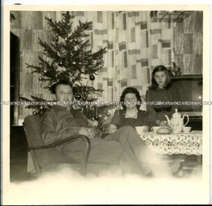 Familienmitglieder am Kaffeetisch vor dem Weihnachtsbaum