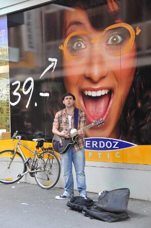 Lausanne - Straßenmusiker : Vor einem großformatigen Werbeplakat in der City spielt ein Straßenmusiker. Aufgenommen am 20. Mai 2010 in Lausanne