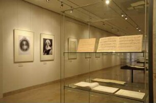 Exponate an der Nord-Wand (Porträts) und Ausstellungsvitrinen mit Partituren