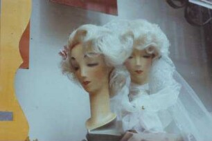 DDR. Zwei weibliche Frisierköpfe, der hintere als Braut dekoriert, im Fenster eines Friseurgeschäftes