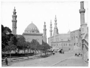 Kairo (Ägypten). Einheimische mit Eselskarren und Pferdekutschen auf einer Straße. Blick zur Sultan-Hassan-Moschee