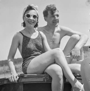 Elisabeth Gremmler (links) und ein befreundeter Mann sitzen auf einem Segelboot, er spielt Mundharmonika