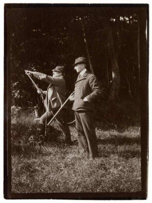 Max Slevogt mit einem Mann vor einem Waldstück, beide mit Jagdgewehren : Max Slevogt mit einem Mann vor einem Waldstück, beide mit Jagdgewehren, Slevogt mit dem Arm auf etwas hinweisend.