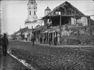 Kriegszerstörte Gebäude : Smederevo, Straßenszene, Blick auf ein zerstörtes Gebäude mit der beschädigten Kirche zum Hl. Großmärtyrer Georg im Hintergrund. Auf der Straße Soldaten.