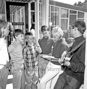 Franz-Spliedt-Heim: Jugendheim des Deutschen Gewerkschaftsbundes (DGB-Nordmark): Seebergen: Internationales Kinderdorf der Deutschen Gesellschaft für internationale Kinderbegegnungen: internationale Kindergruppe im Eingangsbereich eines Heimgebäudes: links Betreuer mit Gitarre