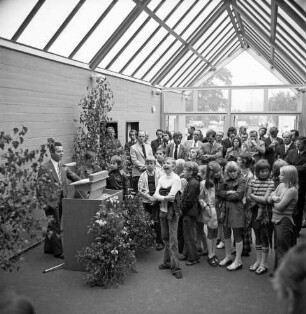 Schulzentrum Reinbek: Mühlenredder: Hauptschule [später: Hertzig-Schule, dann zusammen mit Realschule Reinbek Gemeinschaftsschule Reinbek]: Neubau: Einweihung: Innenansicht: Pausenhalle: Rede des Landesministers für Kultur Walter Braun, am Rednerpult zwischen Grünpflanzen: rechts Schüler, Lehrer und Gäste