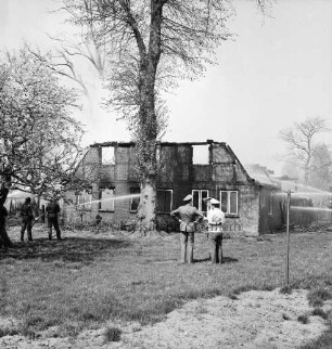Rögen: Brand: Reetdachkate: Ruine mit eingestürztem Dachstuhl: davor Baum: links Feuerwehrmänner beim Löschen: rechts Wasserstrahl von Feuerwehrspritzen: vorn drei Polizisten im Gespräch