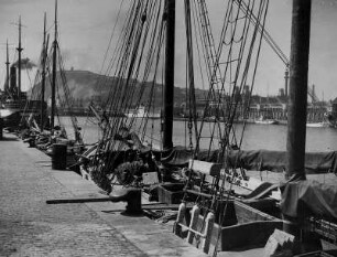 Spanien. Hafenstadt Barcelona. Blick vom Handelshafen zum Tibidabo, einem der Hausberge der Hafenstadt. Am Kai angelegte Segelboote