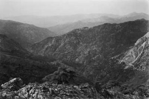 Landschaft : Blick auf die mit Macchie bewachsenen Hochgebirgshänge, dazwischen vereinzelte Zedern, im Tal ein Dorf der Kabylen.