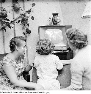 Zwei Frauen mit Kind vor laufendem Fernsehgerät sitzend