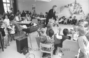 "Alte Schule": Familien-Frühlingsfest: Montessori-Spielkreis bei Musikvortrag: rechts Kinder mit Instrumenten auf Stühlen: in der Mitte Leiterin Brigitte Peters: links Kinder und Erwachsene an Tischen