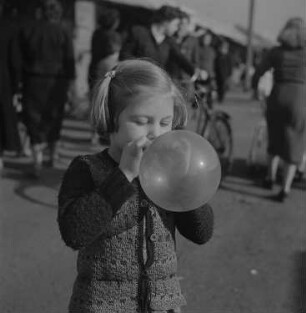 Ein kleines Mädchen bläst auf einer Kleinmesse einen Luftballon