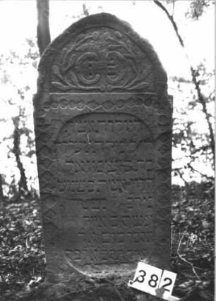 Grabstein 382 (Index: 99898343) Material: Sandstein Zustand: teilweise verwittert Maße HxBxT: 114x57x8 cm Beschreibung: Stele mit eingezogenem Spitzbogenabschluss, im Bogenfeld Blattranken, Schriftfeld gerahmt von Rauten-/Scheibenfries Symbolik: Blattranken, Rauten-, Scheibenfries: Grabstein 382