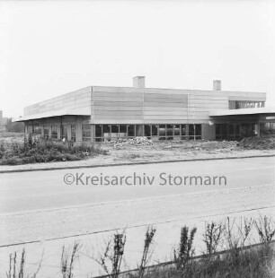 Industriestraße: Firmengebäude im Bau: Rohbau mit Fenstern: davor unbefestigtes Gelände mit Erdhaufen und Baumaterial: 20. Juni 1971