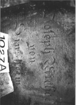 Grabstein 1027 (Index: 99899619) Material: Sandstein Zustand: völlig verwittert, Rückseite stark verwittert Maße HxBxT: 101x66x20 cm Beschreibung: Stele mit eingezogenem Rundbogenabschluss, im Bogenfeld Blüte Symbolik: Blüte: Grabstein 1027A