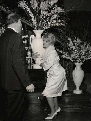[Maria Schell macht Spaß, sie will eine große Vase anheben]