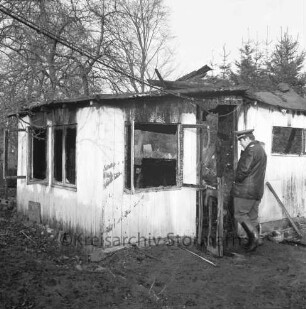 Brand: Sieker Landstraße: Behelfsheim: Brandruine mit eingestürztem Dach: rechts im Eingang Polizist: hinten Bäume
